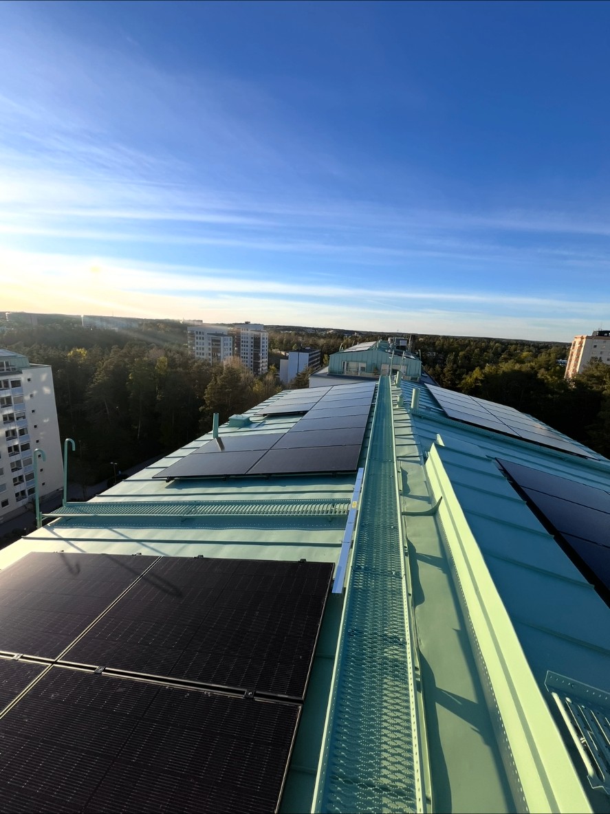 Svarta solcellspaneler på båda sidor om en takbrygga på ett grönt plåttak hos en bostadsrättsförening i Stockholm