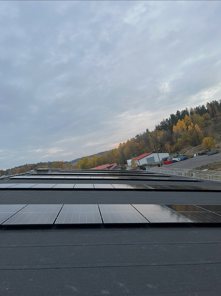 Solcellsinstallation på ishallens tak i Valdemarsvik med omgivande höstskog och en vit byggnad med rött tak intill