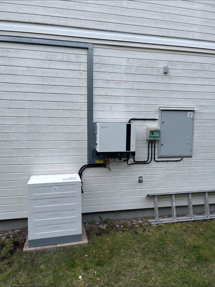 Vitt batteripack och växelriktare monterade på den ljusa träfasaden till en villa i Norrköping, med kabelrännor och elskåp på väggen